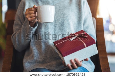 Closeup image of a woman holding a gift box while drinking coffee