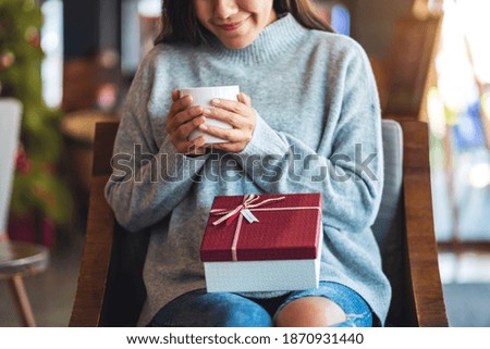 Closeup image of a beautiful young woman holding a gift box while drinking coffee
