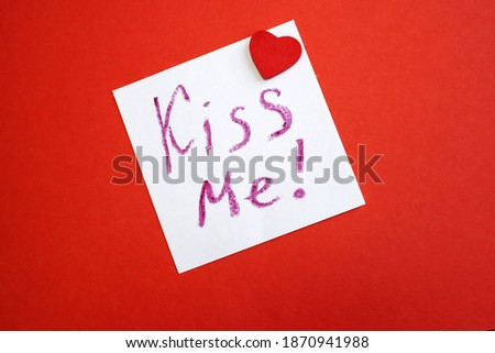 Kiss me is written on a white piece of paper that lies on a red background. Valentine's day