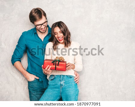 Smiling beautiful woman and her handsome boyfriend. Happy cheerful family posing in studio near gray wall. Valentine's Day. Models hugging and giving his girlfriend gift box. Christmas, x-mas, concept