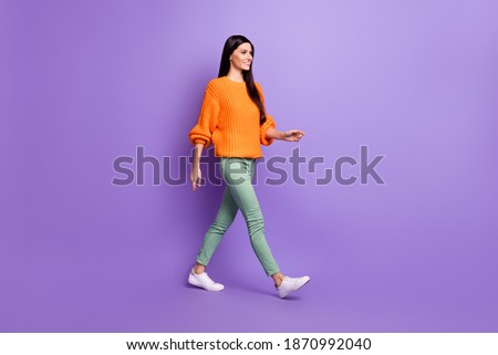 Full length body size photo of young girl walking forward in green pants sweater looking copyspace isolated on vivid purple color background Royalty-Free Stock Photo #1870992040