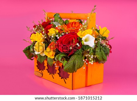 beautiful bouquet of flowers in an orange box with a handle, the background is bright pink