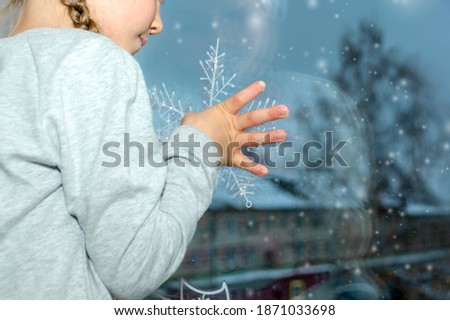 A little girl sticks a decorative Christmas snowflake to the window. We decorate the house for the New Year. Celebrating Christmas at home. close-up