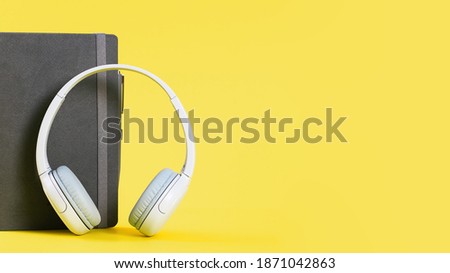 Wireless funky modern gray headphones with diary organizer or notebook on illuminating yellow background. Remote learning or listening to music or radio. Banner with copy space