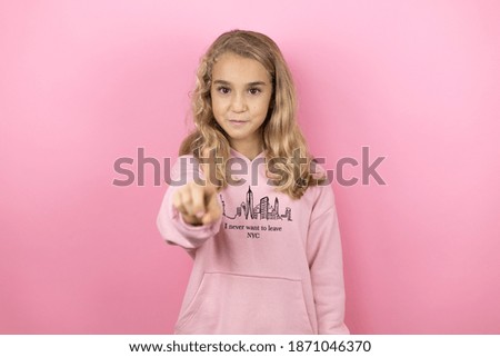 Young beautiful child girl standing over isolated pink background showing and pointing up with fingers number one while is serious