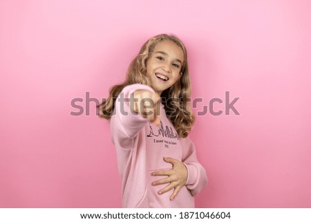 Young beautiful child girl standing over isolated pink background laughing at you, pointing finger to the camera with hand over body, shame expression