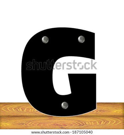 The letter G, in the alphabet set "Construction," is black with silver nails embedded in letter.  Letter sits on wooden planks.
