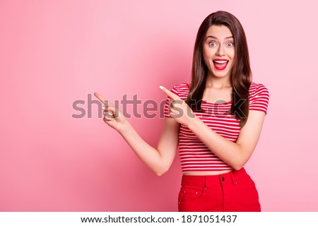 Photo of amazed brown haired girl point fingers empty space wear red striped t-shirt isolated on vivid pink color background