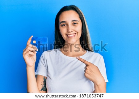 Young hispanic woman holding credit card smiling happy pointing with hand and finger 