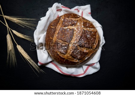 Brown bread with cracked crust wrapped in a cloth from a rough fabric on a background of old tree and scattered flour. Composition in a rustic style, top view.