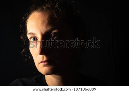 Dark portrait of a serious woman with her face partially lit. The woman is staring blankly showing sadness or anxiety Royalty-Free Stock Photo #1871066089