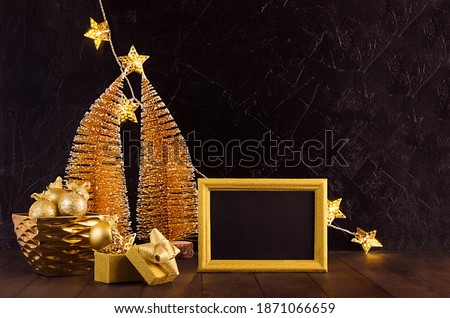 Christmas festive interior with gold christmas trees, glowing lights with stars, blank photo frame, decoration on black plaster wall, brown table.