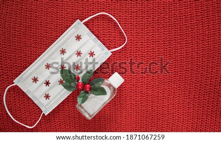 Disposable face mask decorated by snowflakes with sanitizer and christmas decoration on red knitted wool background. Stay safe. Creative concept of Christmas and New Year in new reality. Copy space