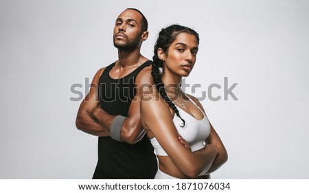 Close up of male and female athlete standing with arms crossed. Couple in fitness wear standing together at the gym. Royalty-Free Stock Photo #1871076034
