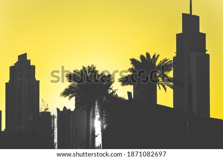 silhouette of city skyscrapers and palm trees on a yellow sunset background.