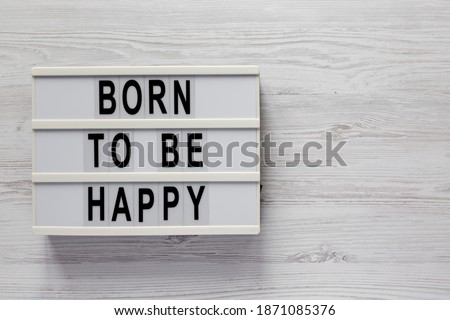 'Born to be happy' on a lightbox on a white wooden surface, top view. Flat lay, overhead, from above. Space for text.