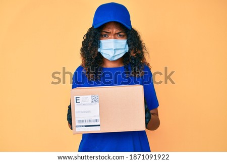 Young african american woman wearing medical mask holding delivery package skeptic and nervous, frowning upset because of problem. negative person. 