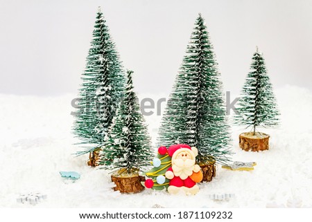 Small decorative Christmas trees with New Year's decor. Santa Claus, snowflakes, shining stars and artificial snow on white putty background, copy space