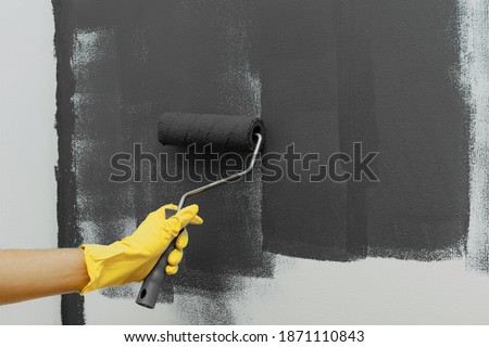 Strips of gray paint on a white wall and man's hand in yellow glove with a roller. Home renovation, texture. Copy space. Trendy color of 2021 year.