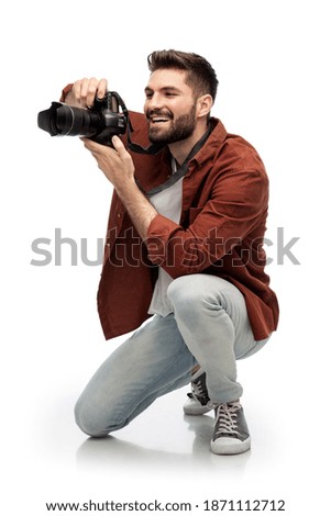 photography, profession and people and concept - happy smiling man or photographer with digital camera staying on one knee and taking picture over white background
