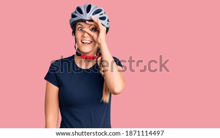 Beautiful caucasian woman wearing bike helmet doing ok gesture with hand smiling, eye looking through fingers with happy face. 