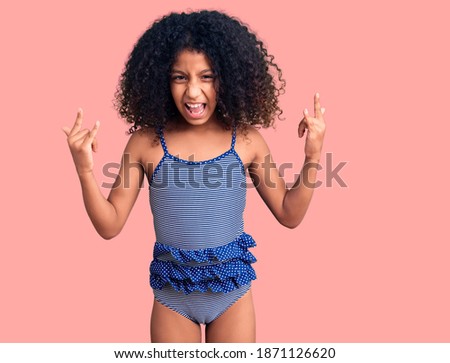 African american child with curly hair wearing swimwear shouting with crazy expression doing rock symbol with hands up. music star. heavy concept. 