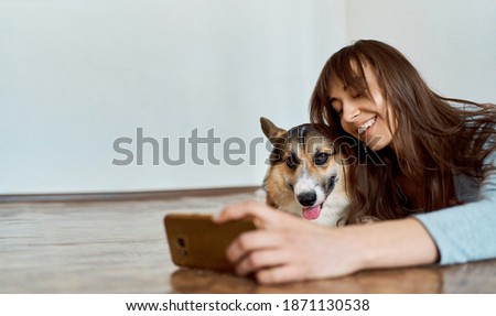 Woman with charming smile lying on floor in living room with pet and making selfie photo. Spend time together at home. Focus on dog