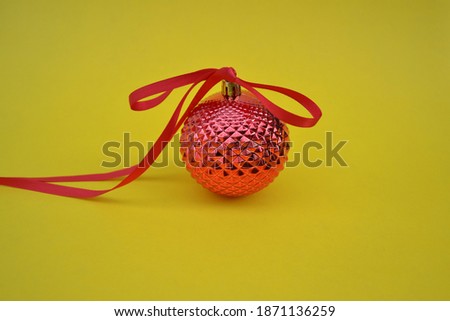Red Christmas ball with ribbons on a yellow background, copy space. Elegant and minimal concept.