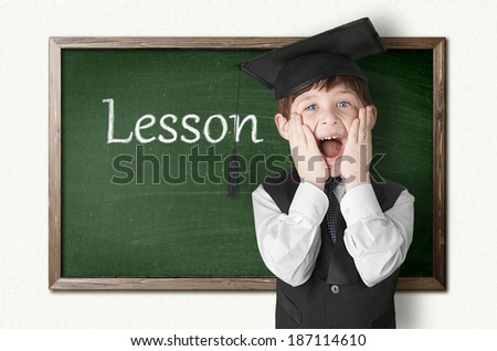 Cheerful little boy on blackboard. Looking at camera