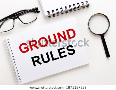 GROUND RULES is written in a white notebook on a light background near the notebook, black-framed glasses and a magnifying glass.