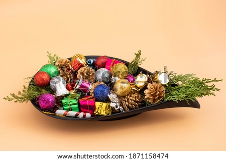 Collection Of Colorful Xmas Decoration Ornaments Like Conifer Pine Cones Glitter Balls Gift Boxes Drums Green Fur Leaves Decorated In Designer Black Pot On Beige Color Background