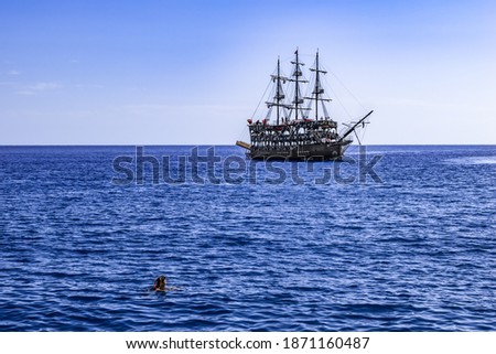 A person in a Scuba Diving Mask in the Mediterranean Sea looks at a vintage pirate ship with three masts in Alanya (Turkey). Seascape with a swimmer in blue water and a schooner on the horizon