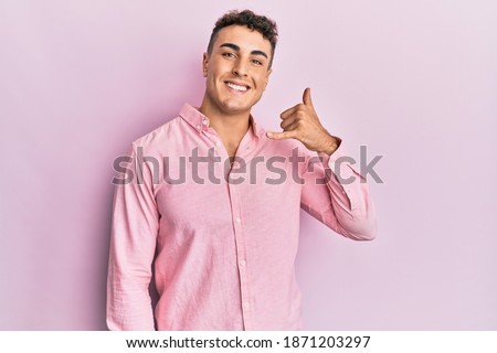 Hispanic young man wearing casual clothes smiling doing phone gesture with hand and fingers like talking on the telephone. communicating concepts. 