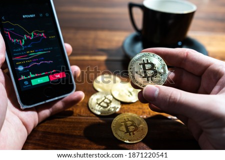 Smartphone with Bitcoin trading chart on the screen. Holding in hand a gold Bitcoin Cash coin. Trading on the cryptocurrency exchange. Royalty-Free Stock Photo #1871220541