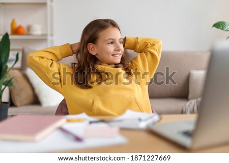 Happy smart school girl sitting in front of laptop, resting after online class with school teacher, finished her homework, got excellent mark at lesson, looking at window. Homeshooling, home education Royalty-Free Stock Photo #1871227669