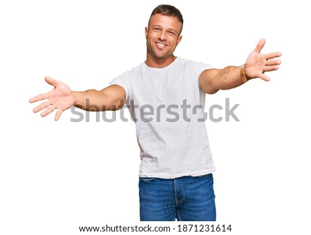 Handsome muscle man wearing casual white tshirt looking at the camera smiling with open arms for hug. cheerful expression embracing happiness. 