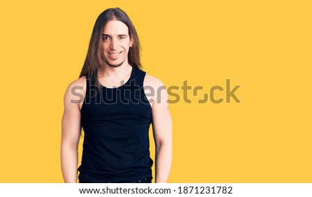 Young adult man with long hair wearing goth style with black clothes with a happy and cool smile on face. lucky person. 