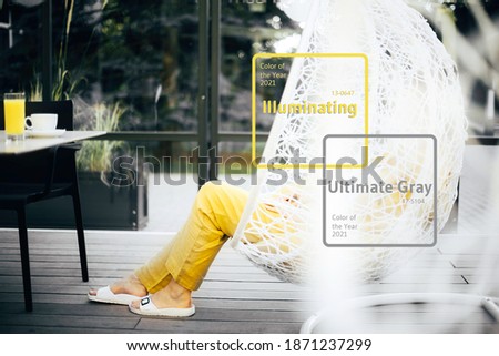 Illuminating and Ultimate gray duotone picture. Style girl, yellow clothes chilling out in hanging wicker chair. Minimalistic style outdoor interior. Demonstrating trendy Color of the Year 2021.