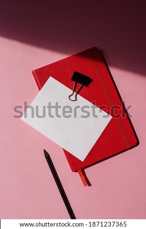Workspace with paper letterhead, pencil and red notebook on pink background. Flat lay. Top view office desk. Branding identity. Add your text.