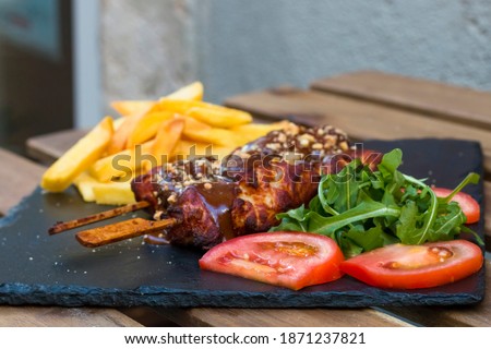 American fast food. A couple of beef and chicken skewers with a delicious peanuts sauce with some fresh salad with tomatoes and crunchy french fries. Delicious meat steaks on a wooden background.