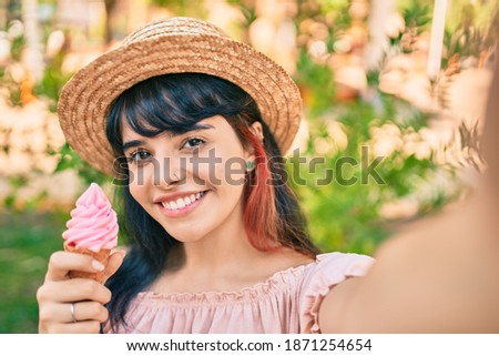 Young hispanic tourist girl wearing summer style eating ice cream and making selfie by the camera at the park.