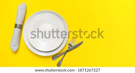 Minimalist table setting in the trendy colors  - Yellow and Gray. grey plates fork knife napkin on yellow background. 