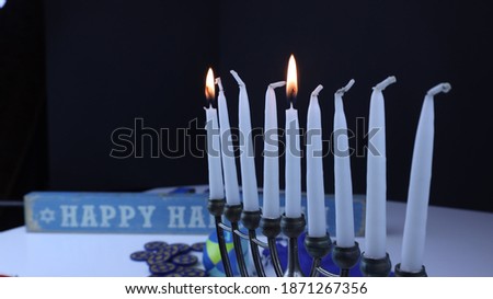 Chanuka candles with shamash lit and the first candle with Star of David coins and decorations