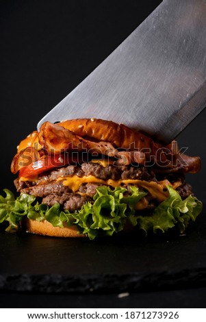 A vertical shot of a big burger and a cleaver knife on a black background