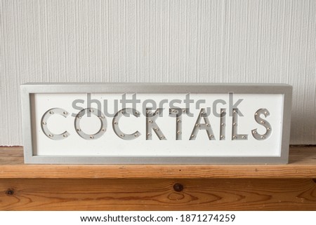 Light up sign saying cocktails on a wooden shelf, illuminated.