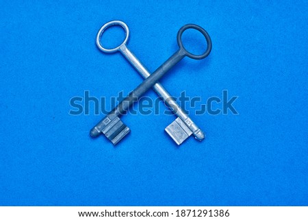 A top view of two crossed metal keys on blue surface