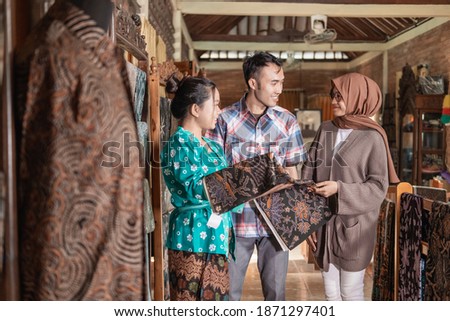 a woman showing the traditional batik cloth she sells to customer Royalty-Free Stock Photo #1871297401