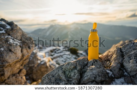Yellow outdoor travel water bottle. Male hand holding bottle. Mountains and winter in national park in during sunset. Travel concept, drink water, adventure   Royalty-Free Stock Photo #1871307280