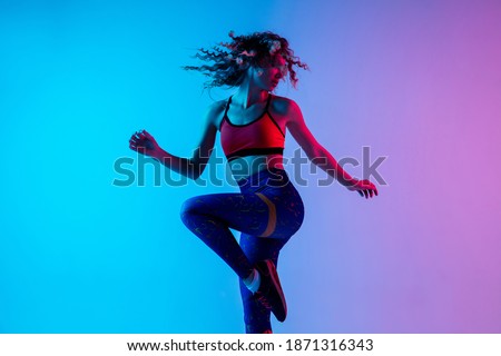 Sport dancing. Beautiful woman in bright sportwear isolated on gradient pink-blue background in neon light. Athletic and graceful. Modern sport, action, motion, youth concept. Female practicing Royalty-Free Stock Photo #1871316343