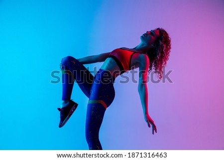 Break. Young beautiful woman in bright sportwear isolated on gradient pink-blue background in neon light. Athletic and graceful. Modern sport, action, motion, youth concept. Sportive female practicing Royalty-Free Stock Photo #1871316463